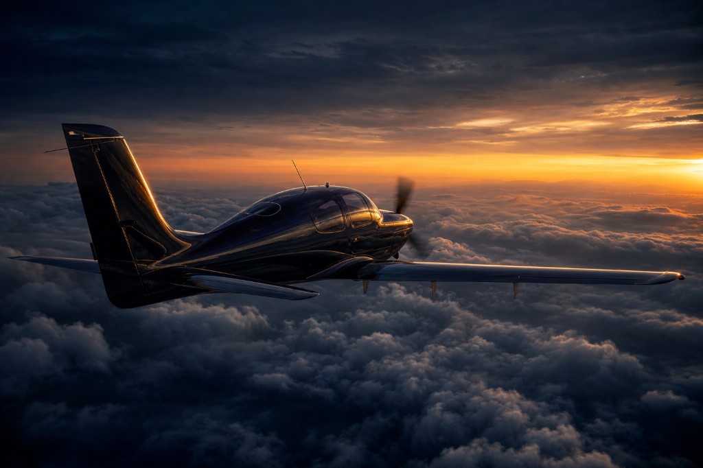 Dark-painted SR22T banking above a sea of clouds at sunset, golden light on the fuselage